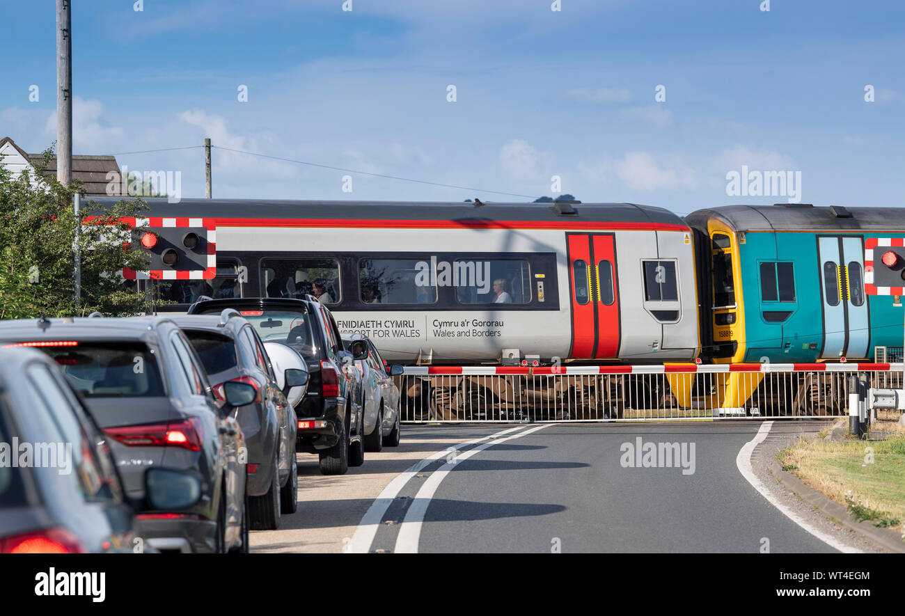 Cars queuing up at a level crossing as a train passes. Wales, UK. Stock Photo
