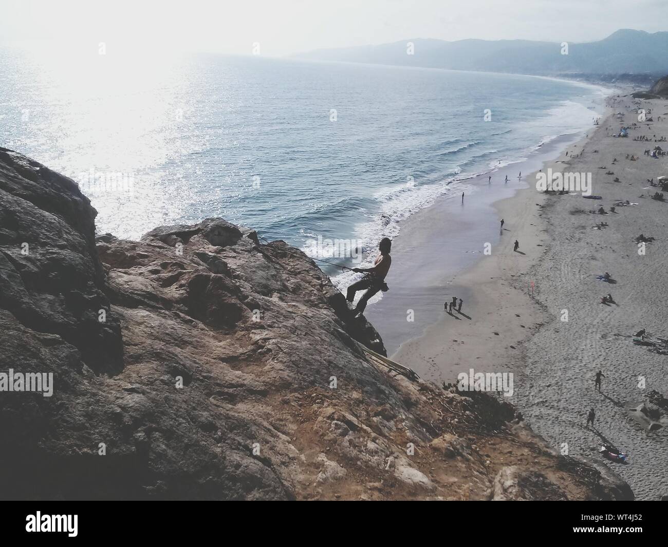 Man Climbing On Cliff By Sea Stock Photo