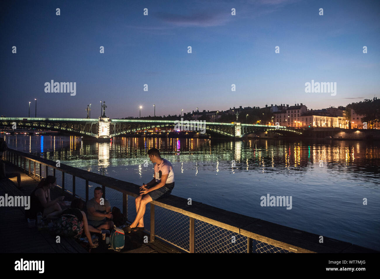 LYON, FRANCE - JULY 18, 2019: French people, mainly men sitting on the riverbank of the Rhone (quais) in the evening drinking alcohol while people are Stock Photo