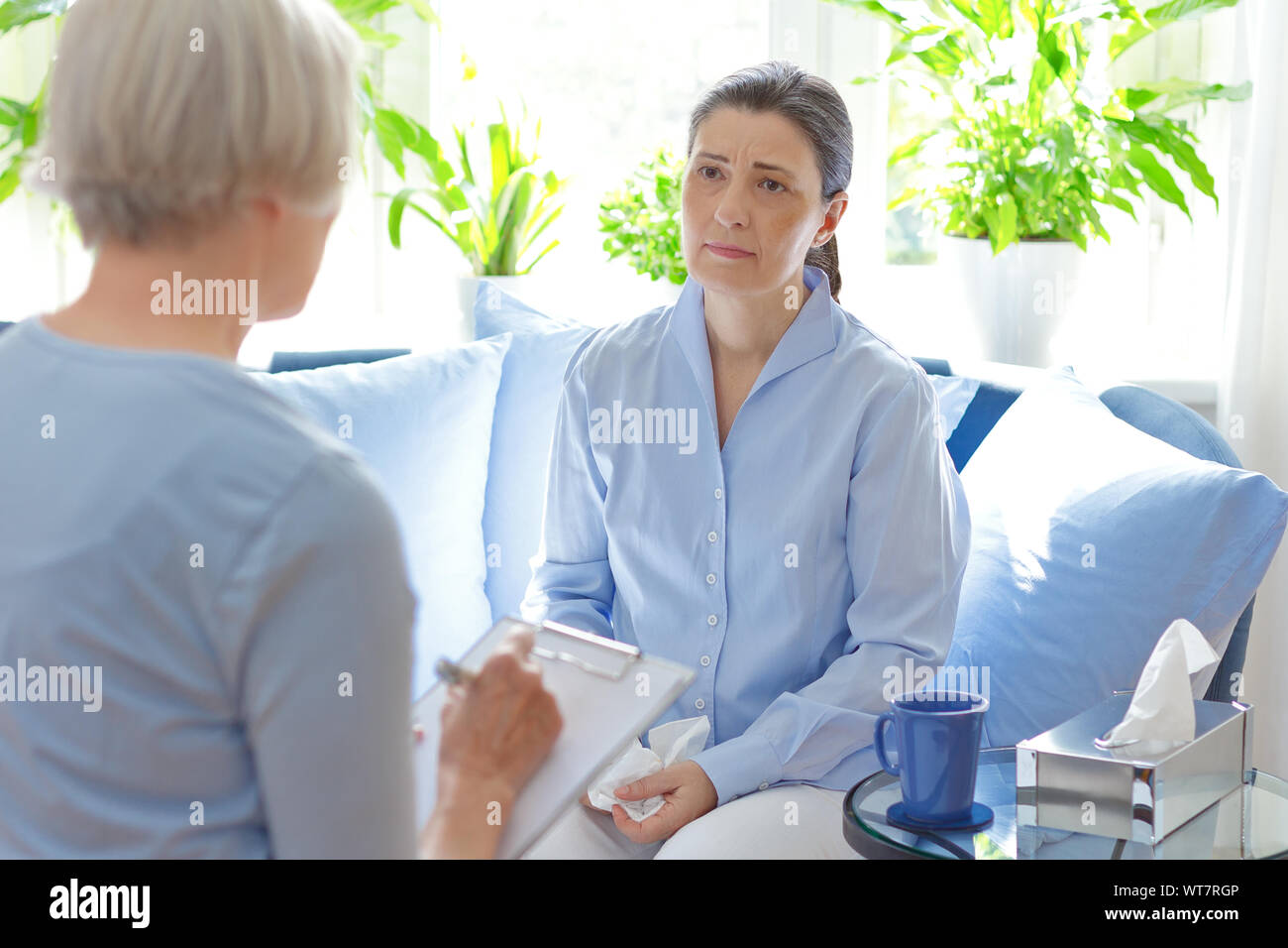 Counseling concept: psychotherapist taking notes during a therapy session with her sad middle aged client. Stock Photo