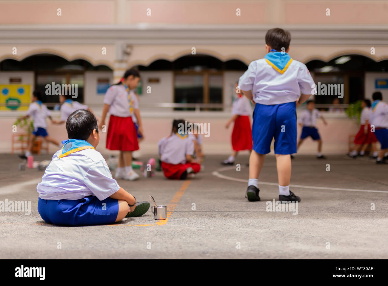 Fat boy lonely sitting in school playground watching friend playing Stock Photo