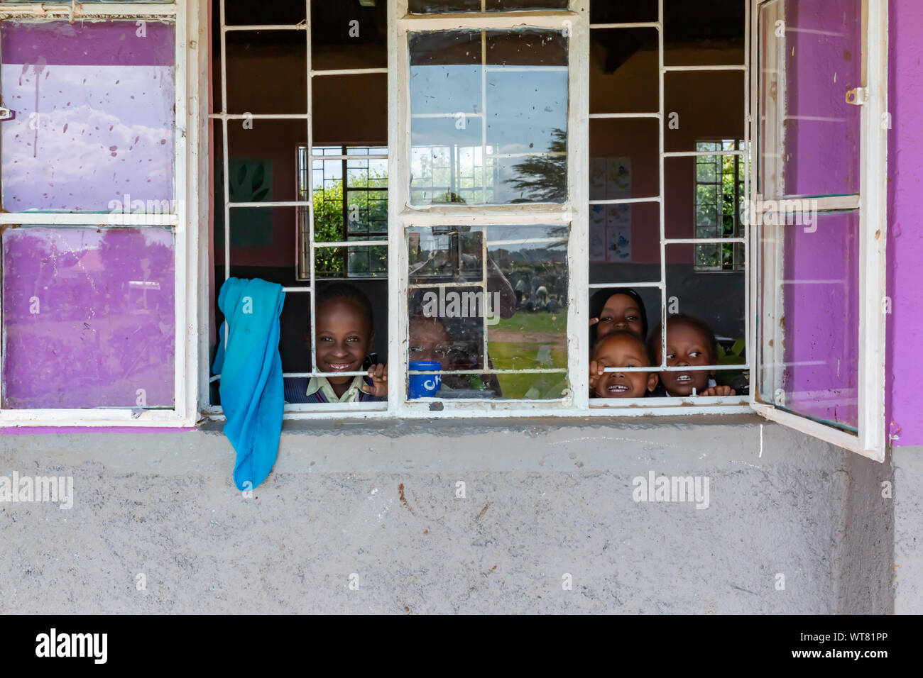 Imani Junior Academy, Nanyuki, Laikipia county, Kenya – June 13th, 2019: Young African school children peeking out of open window from class room with Stock Photo