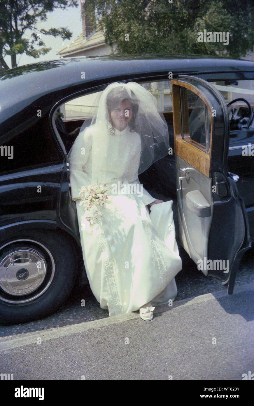 1970s, historical, a bride in her wedding dress and veil getting out of the rear of wooden panelled bridal car, England UK. Stock Photo