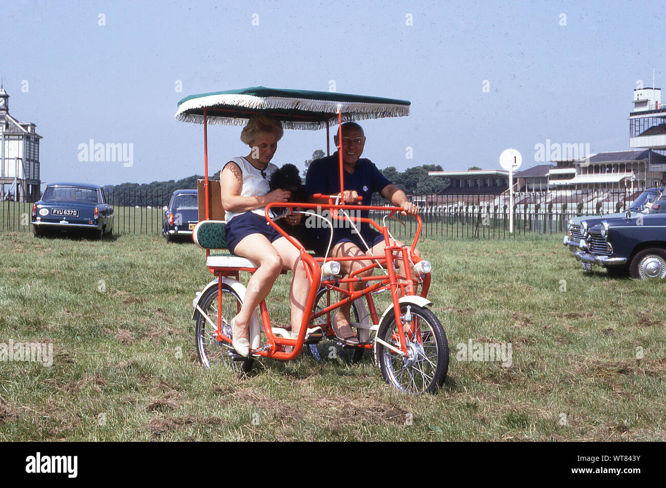 1960s, historical, at York Racecourse, an adult couple sitting on an orange coloured two-seater tricycle at the annual CTC Rally, England, UK. Stock Photo