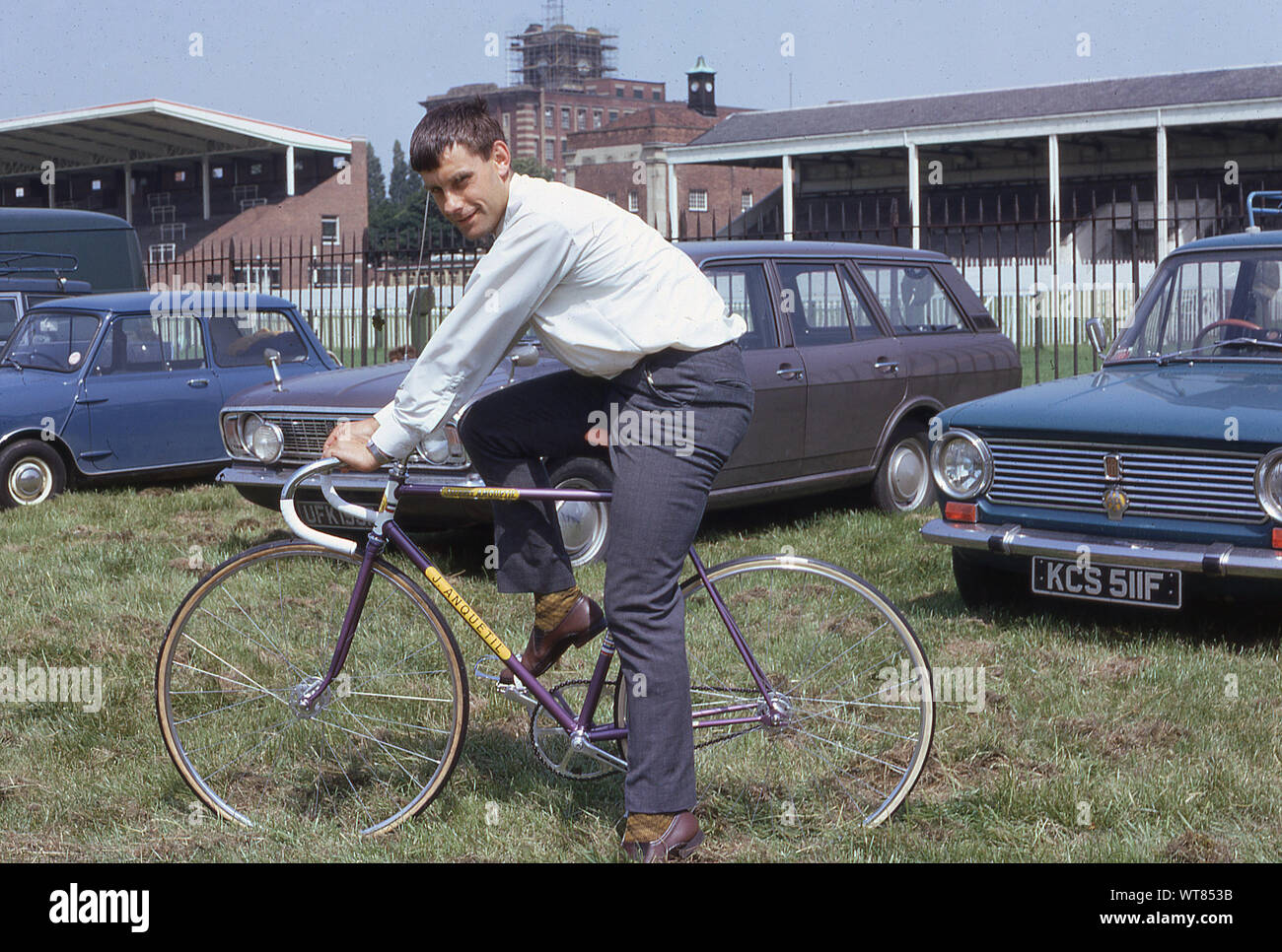 1960s, historical, a male cyclist sitting on a 'J. Anquetil' track bicycle at the York race course during the CTC rally, England, UK. Cars of the era, a Ford Cortina, British Leyland Mini and an Italian 'Fiat' can be seen in the picture. Stock Photo