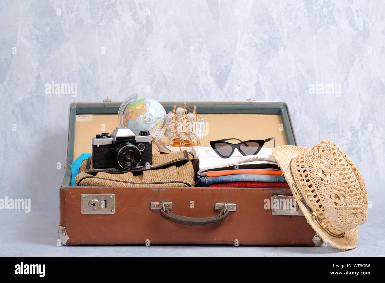 Full travel suitcase on grey background, opened case with travel clothing and accessories. Travel or tourism, vacation, holiday concept Stock Photo