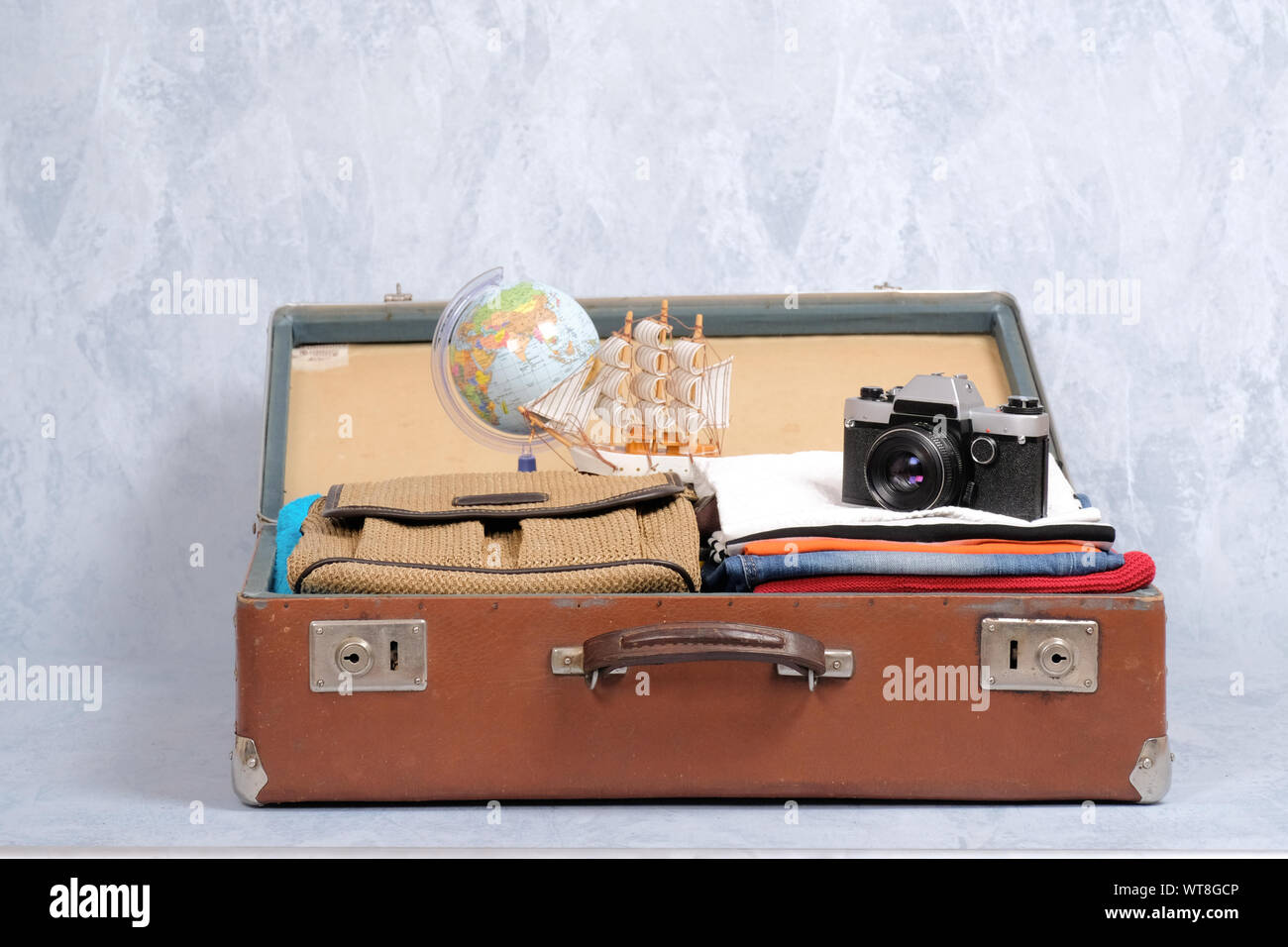 Full travel suitcase on grey background, opened case with travel clothing and accessories. Travel or tourism, vacation, holiday concept Stock Photo