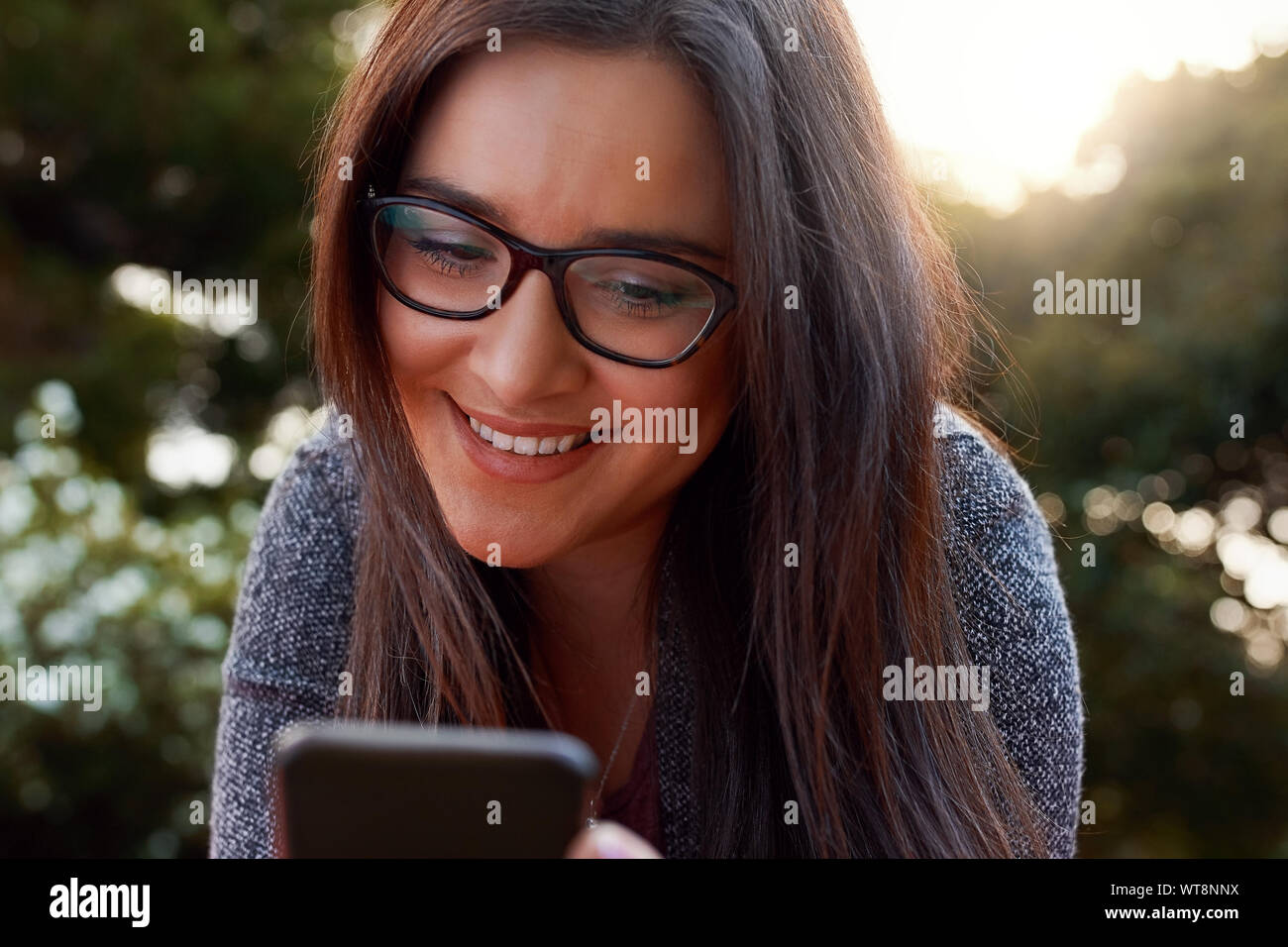 Close-up of smiling young woman wearing black eyeglasses using smart phone at outdoors Stock Photo