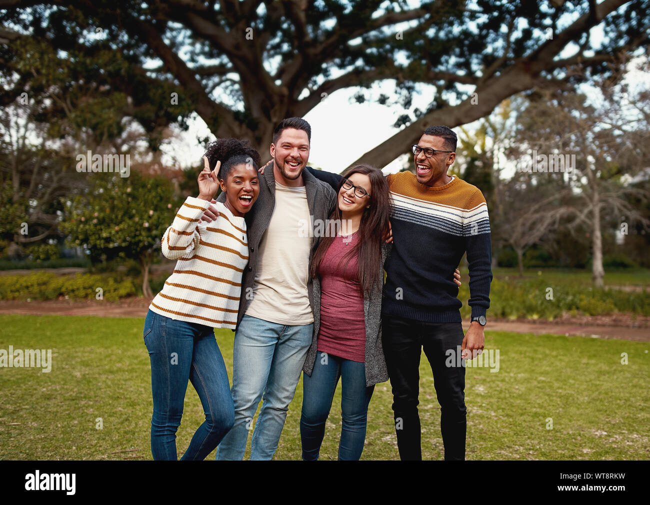 Multiracial group of friends enjoying and standing together in the park looking at camera smiling - very colorful clothing Stock Photo