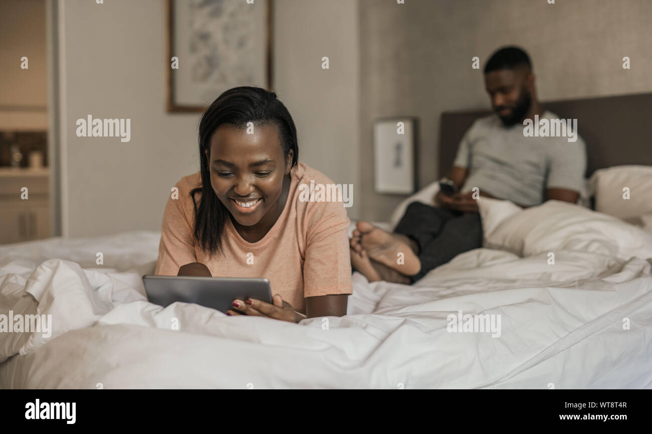 Smiling African American woman lying in bed using a tablet Stock Photo ...