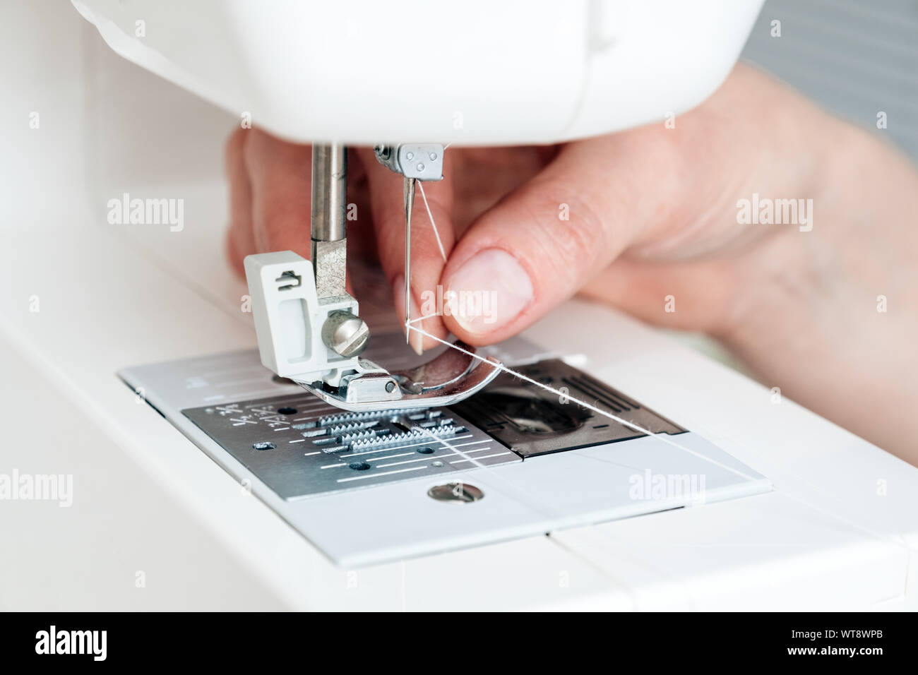 Woman's hand holding thread and threading a sewing machine needle
