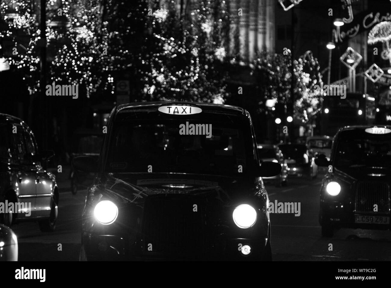 AUTHENTIC BLACK AND WHITE  IMAGE OF LONDON TAXI CABS WORKING IN OXFORD STREET, LONDON AT NIGHT OVER THE CHRISTMAS HOLIDAY PERIOD. CHRISTMAS DECORATIVE STREET LIGHTS ALONG THE STREET. MONOCHROME IMAGES. STREET LIFE. CITY LIFE. URBAN SCENE AT NIGHT. CHRITMAS. Stock Photo