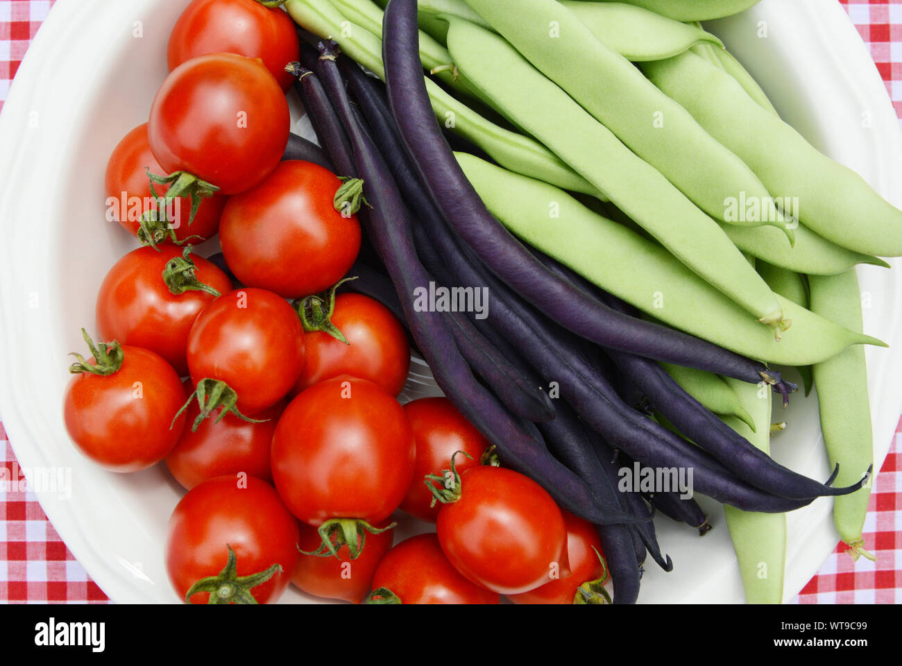 Juicy cherry tomatoes with purple French beans and green Calypso beans in a serving dish - seen from above Stock Photo