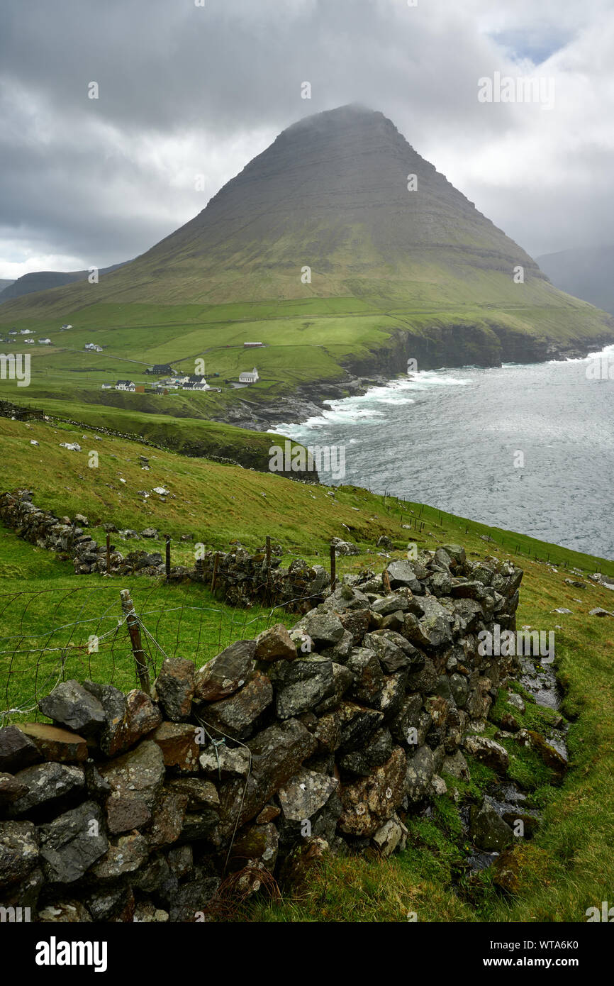 Stone ridge leading to mountain peak along green seashore washing by ...