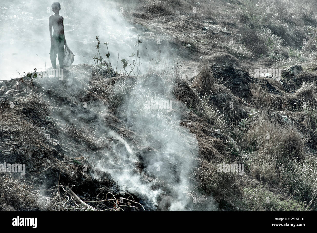 Young boy behind the smoke of the Stung Meanchey landfill Stock Photo