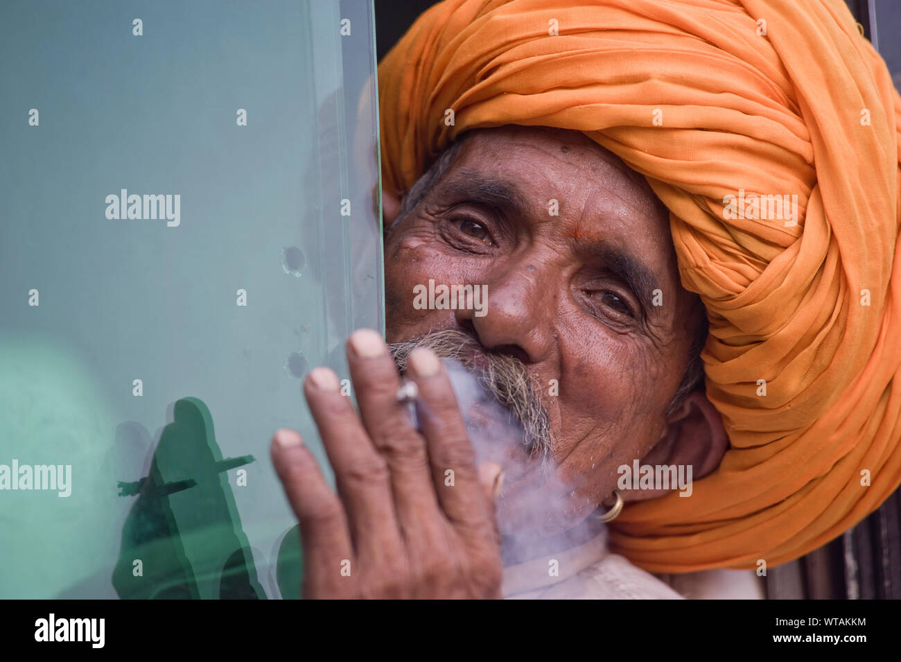 RajasthanÂ´s man with big orange turban smokes in the bus window Stock Photo