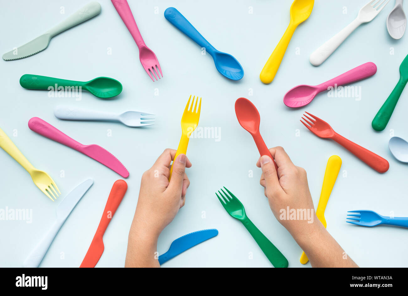 Top view of hand holding colorful spoon and fork with another element on color table.flat lay design Stock Photo