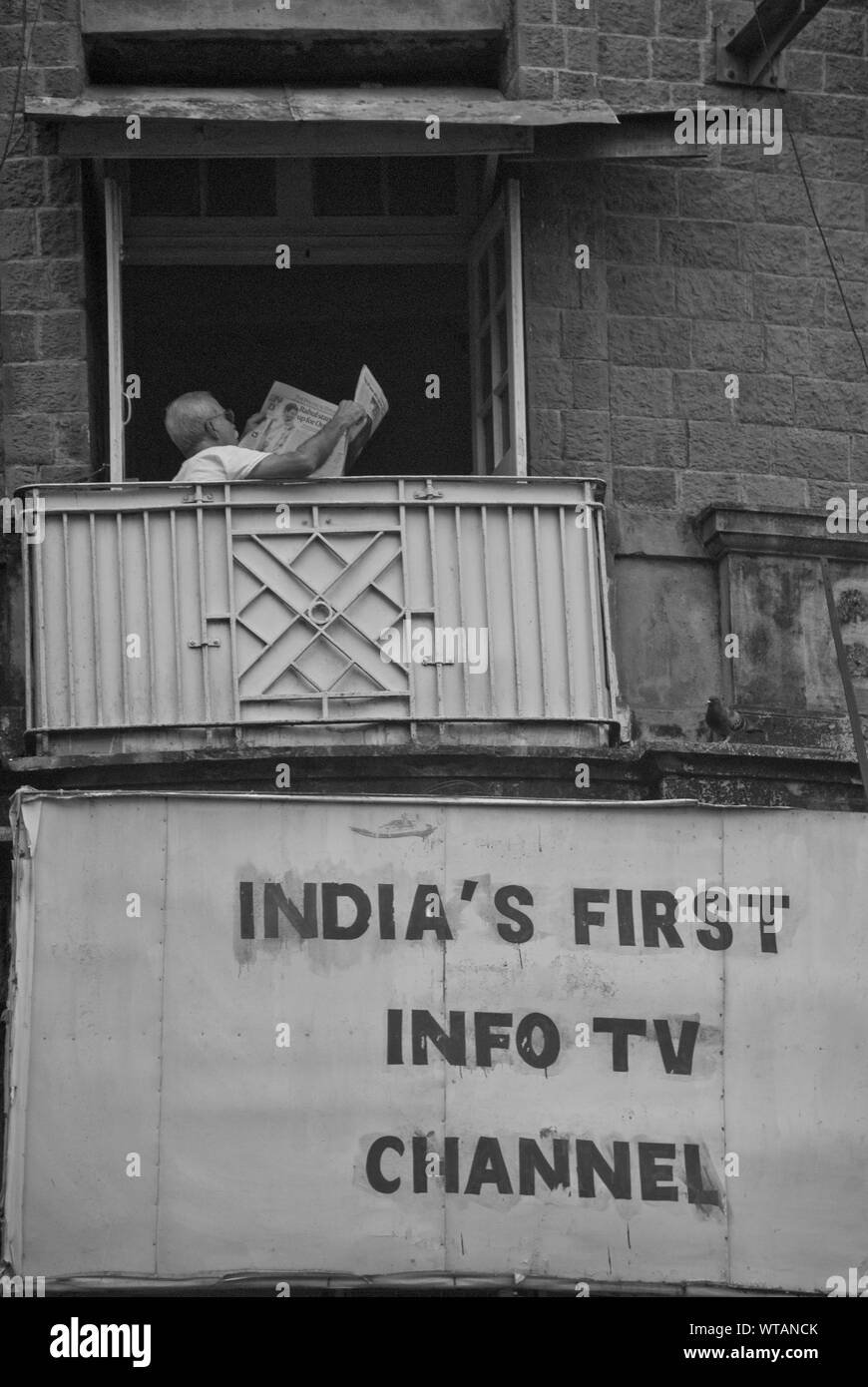 Man reading newspaper in a balcony on Mumbai downtown Stock Photo
