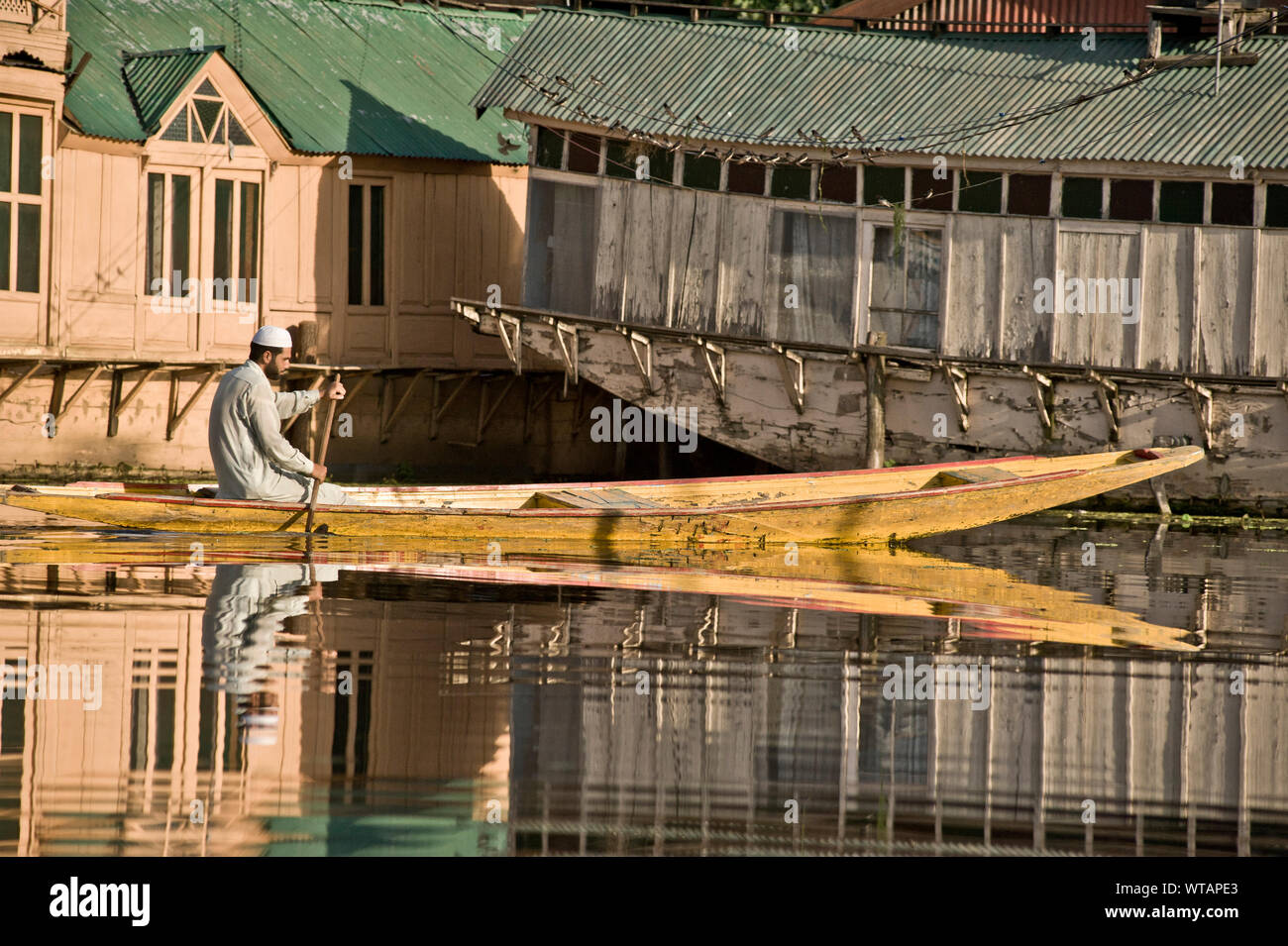 Muslim man paddles yellow boat on Dal Lake Stock Photo
