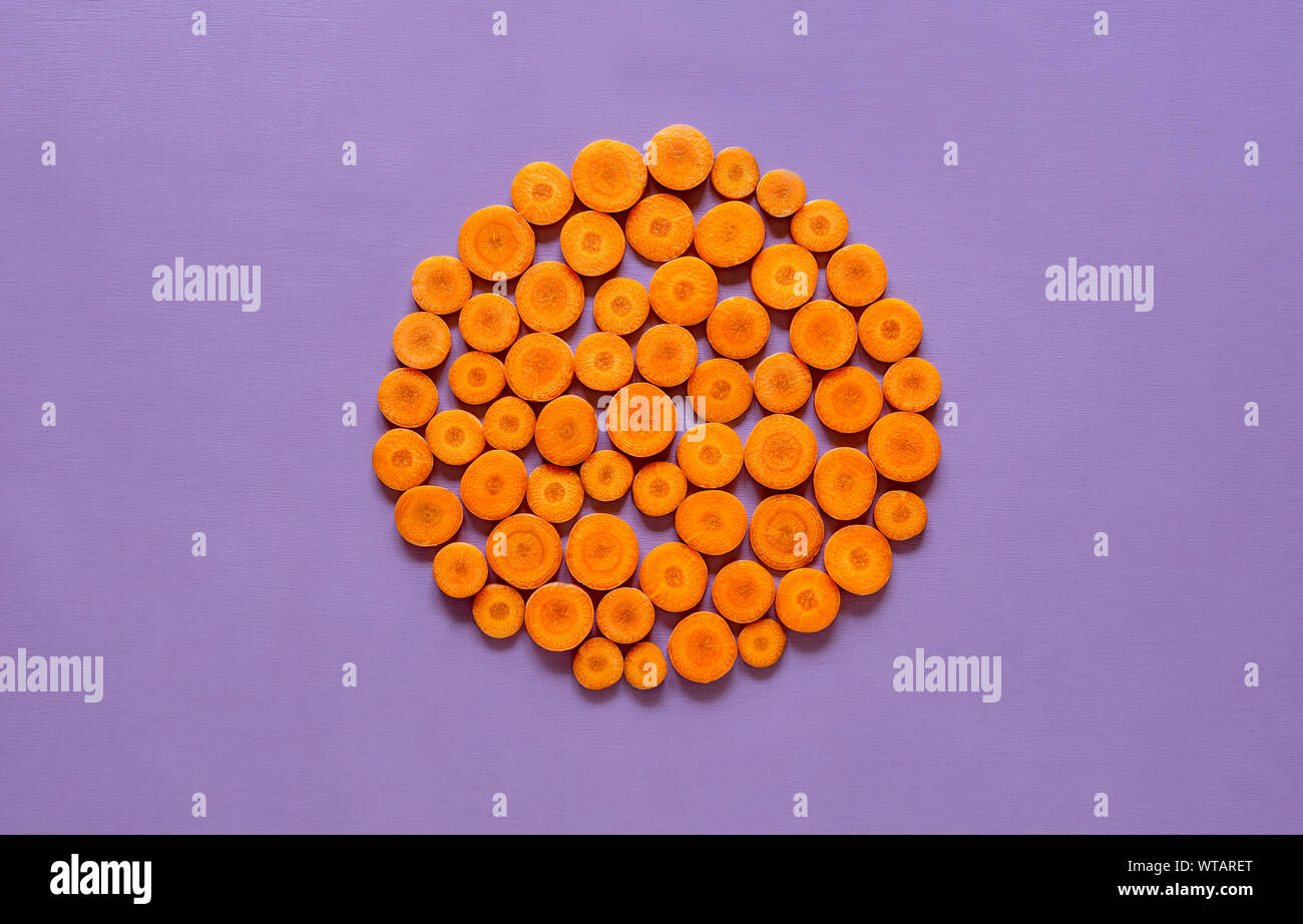 Orange carrots sliced and displayed in a round form on a purple tabletop. Above view of fresh carrots background. Vitamin A vegetable concept. Stock Photo
