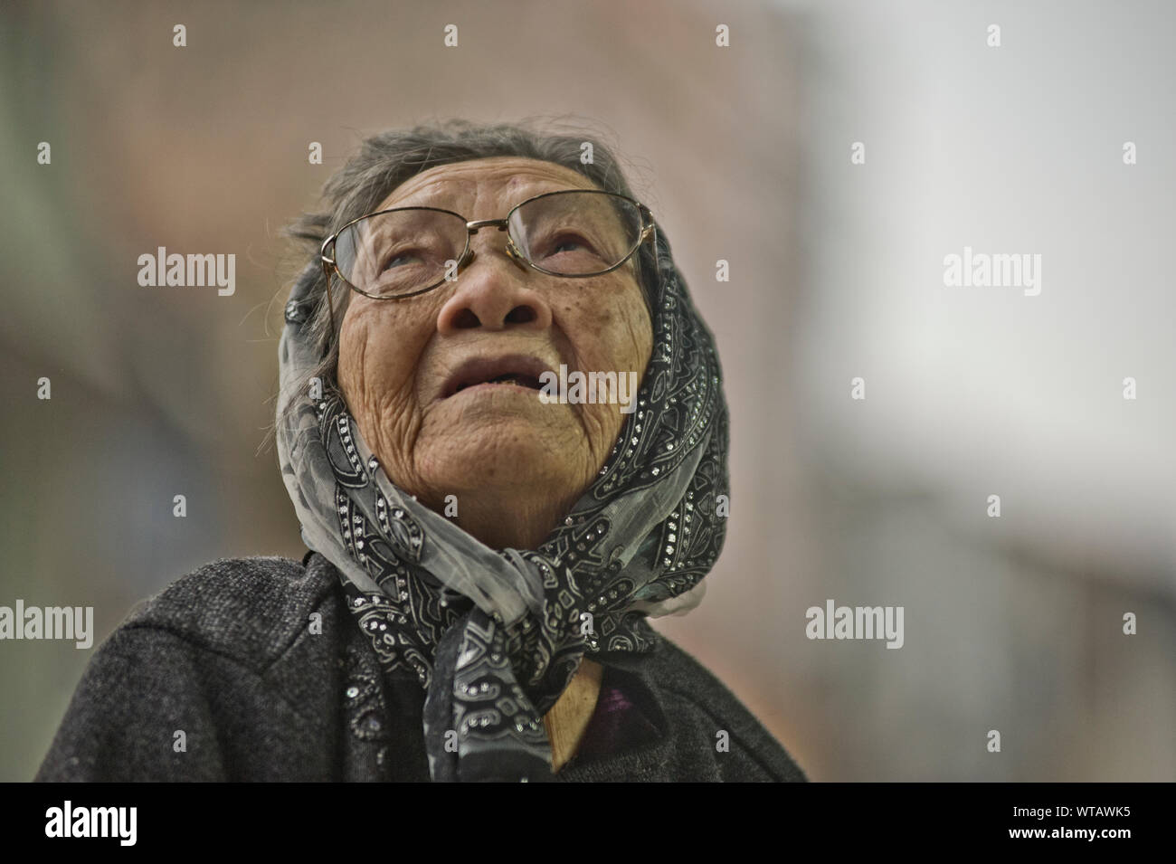 Old woman wears a headscarf and looks up Stock Photo