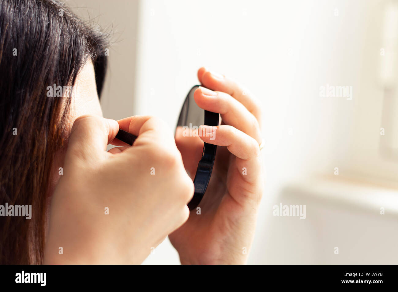 Female person using tweezers and a mirror with natural light. Personal