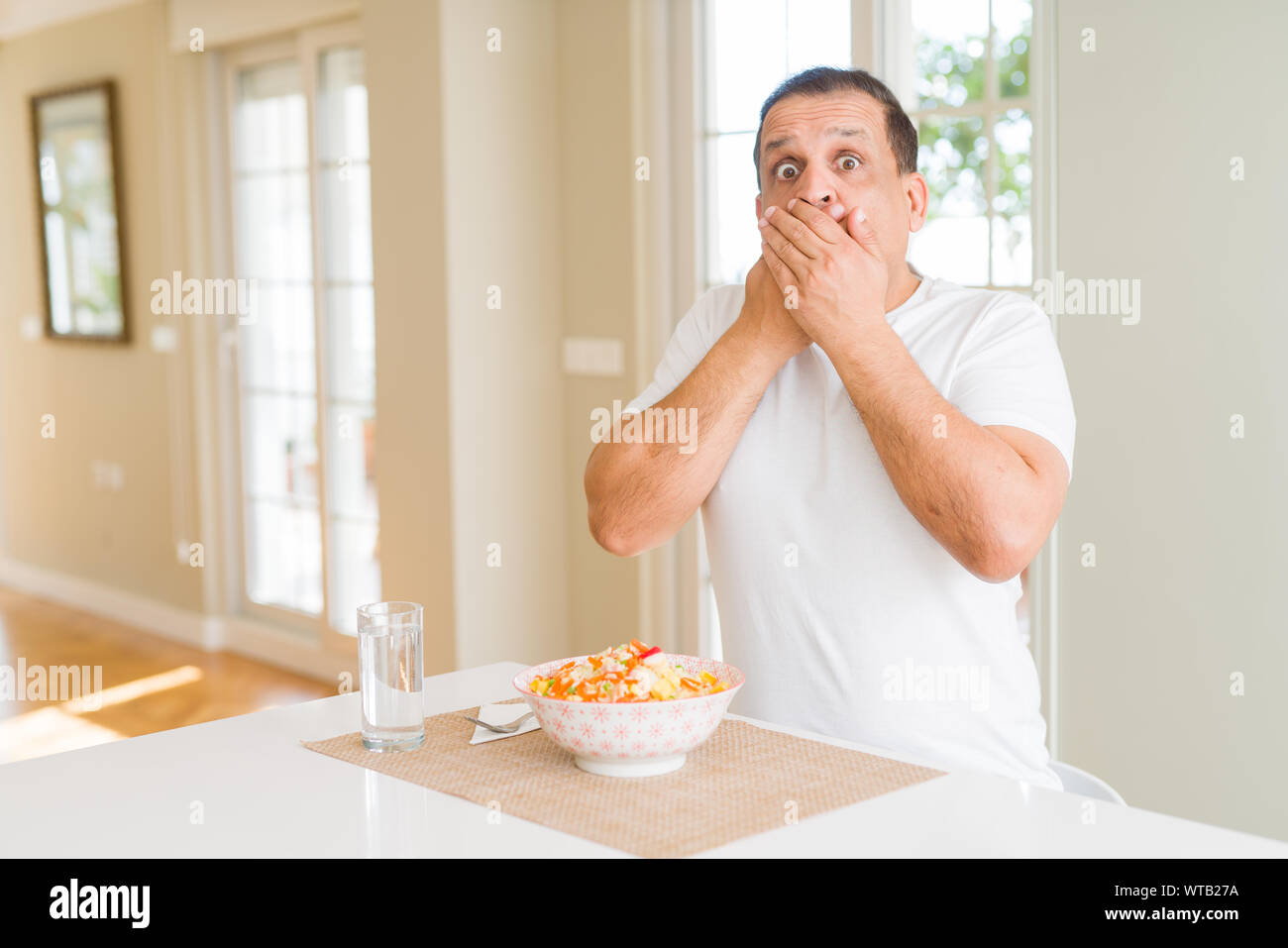 Middle age man eating rice at home shocked covering mouth with hands ...