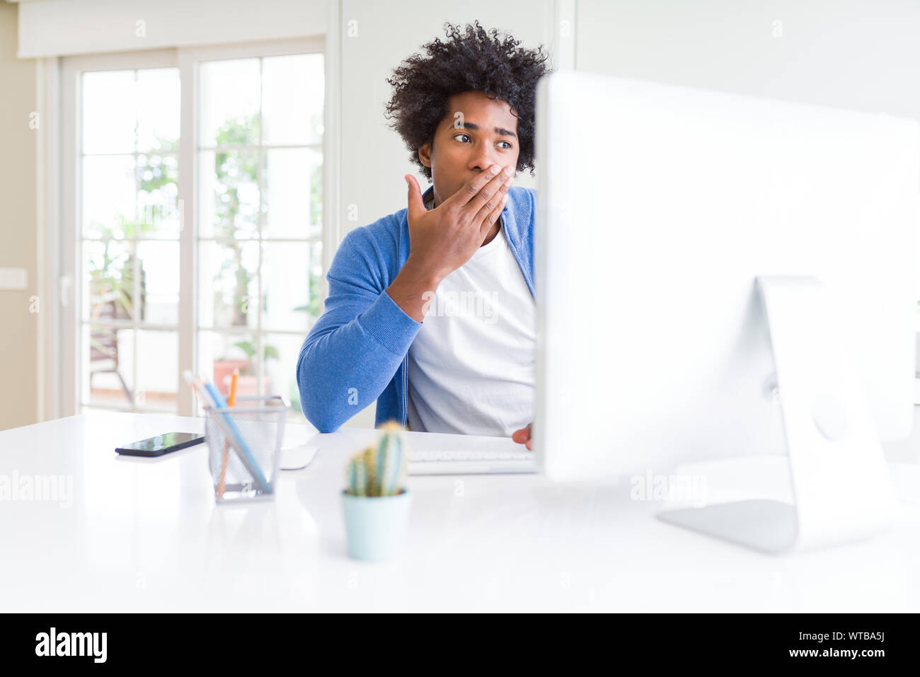 African American man working using computer cover mouth with hand ...