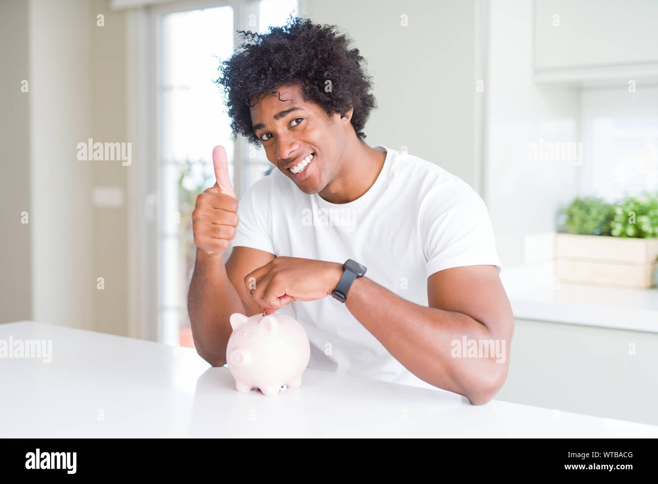 African American man putting a coin inside piggy bank happy with big ...