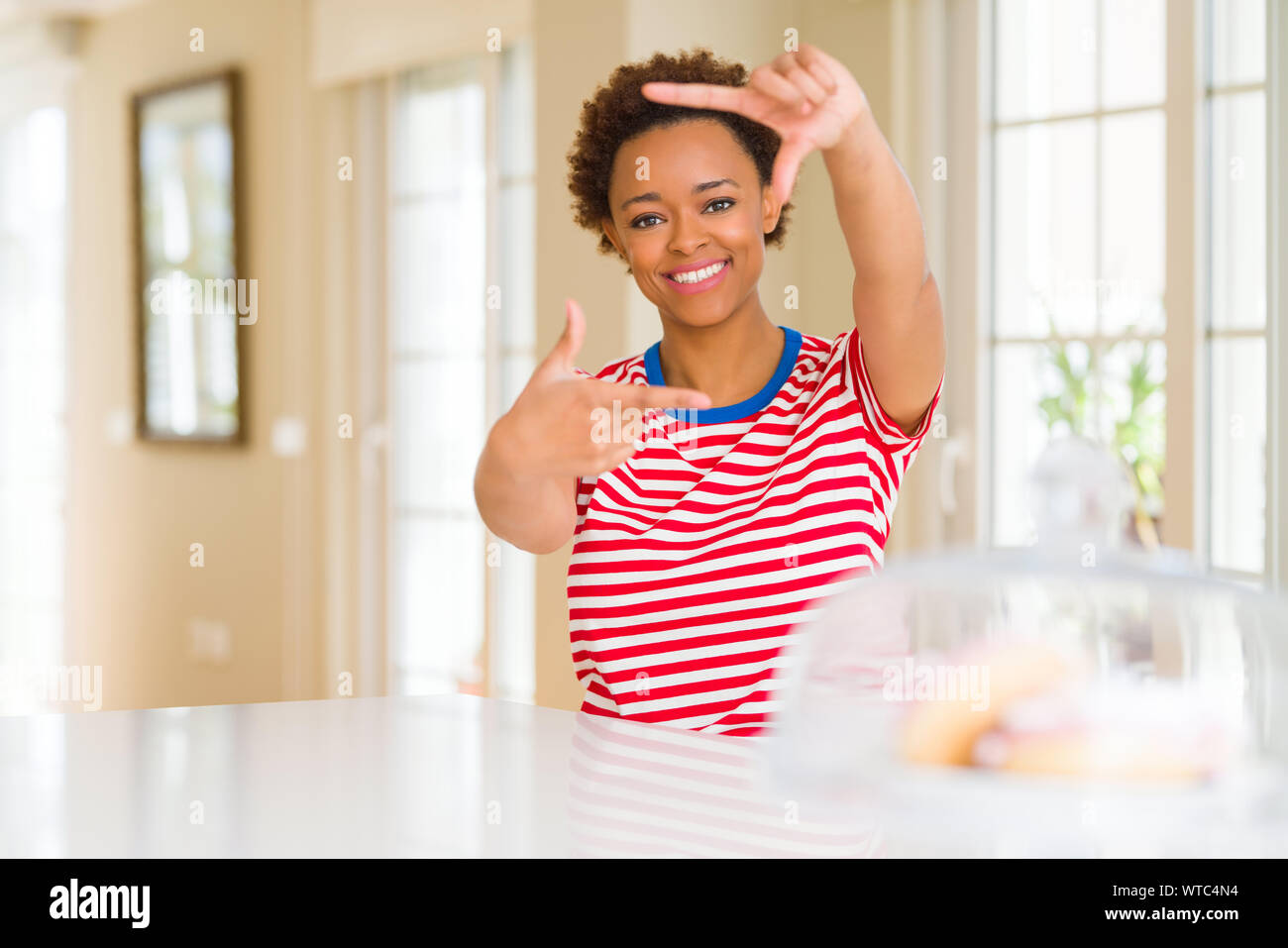 Young beautiful african american woman at home smiling making frame ...