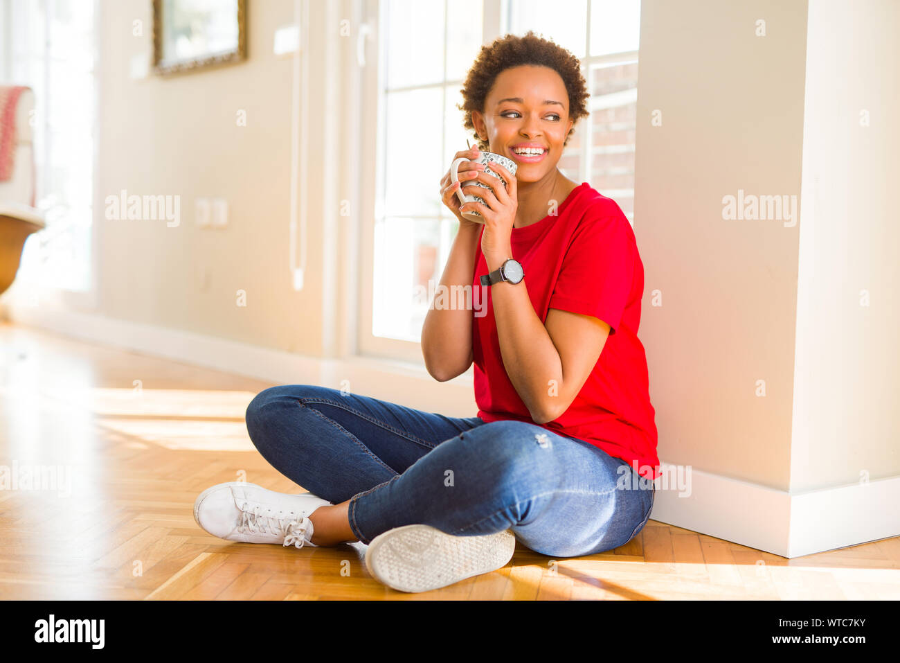 Beautiful young african american woman sitting on the floor at home and ...