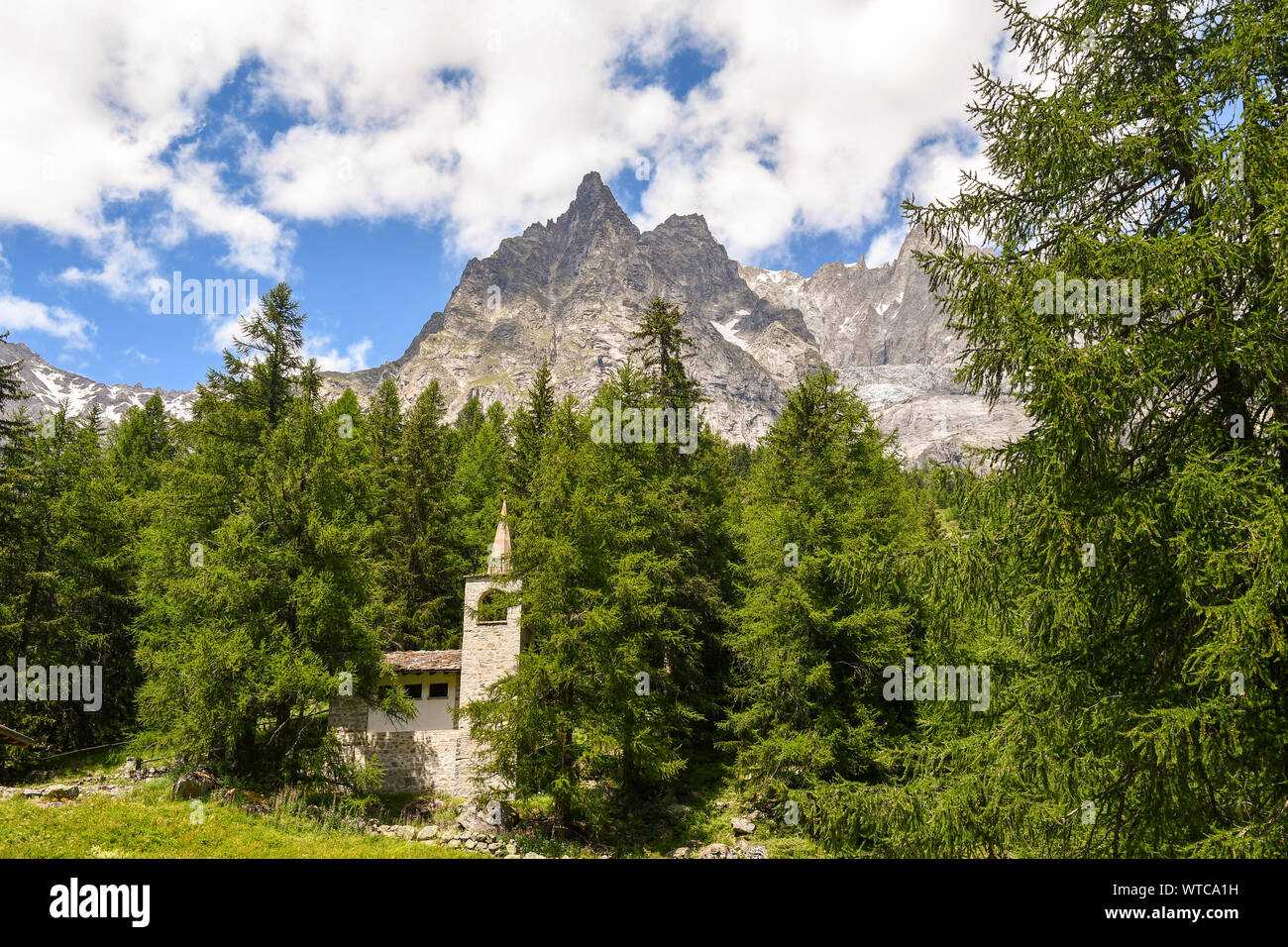 Alpine mountain landscape with a stone church in a pine forest at the foot of the Mont Blanc range in summer, Val Ferret, Courmayeur, Aosta, Italy Stock Photo