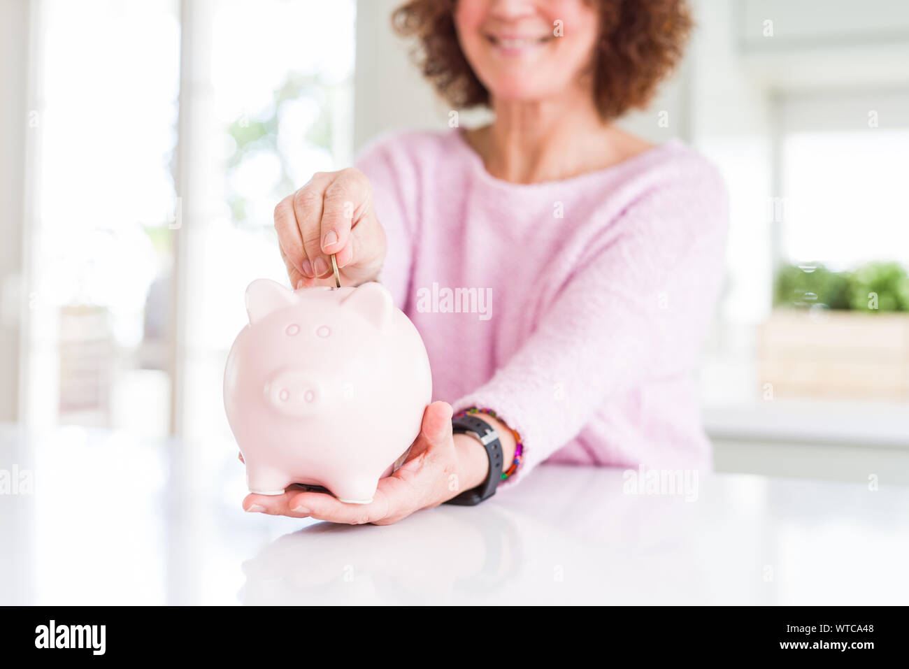 Close up of senior woman putting a coin inside piggy bank as savings ...