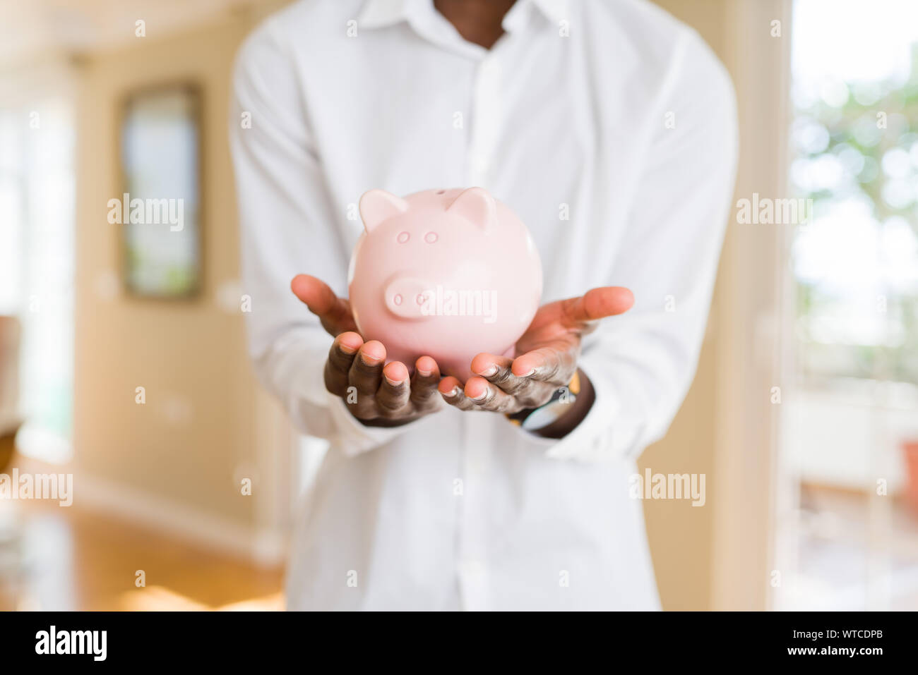 Close up of african man holding piggy bank with hands protecting and ...