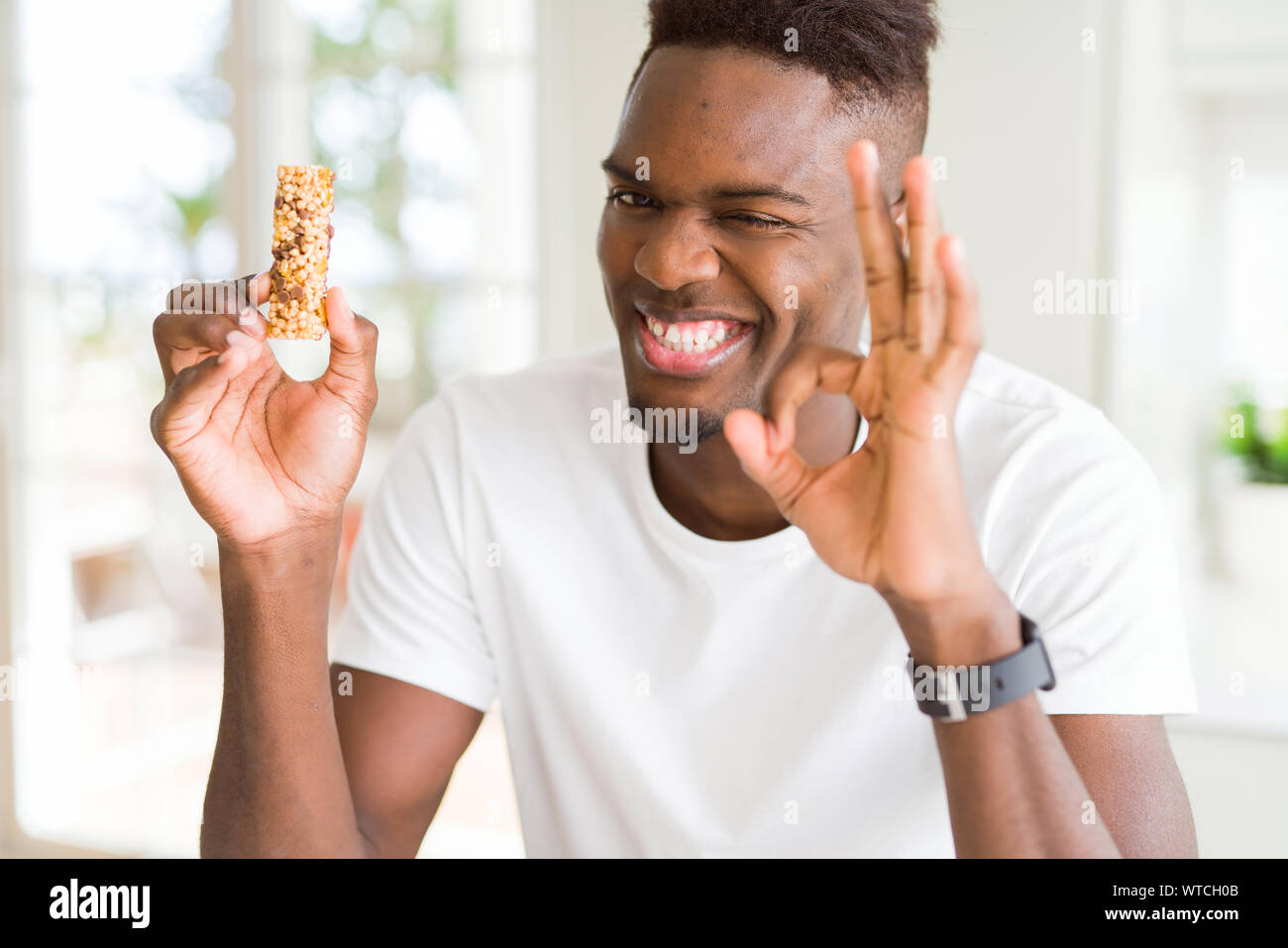 African american man eating energetic cereals bar doing ok sign with