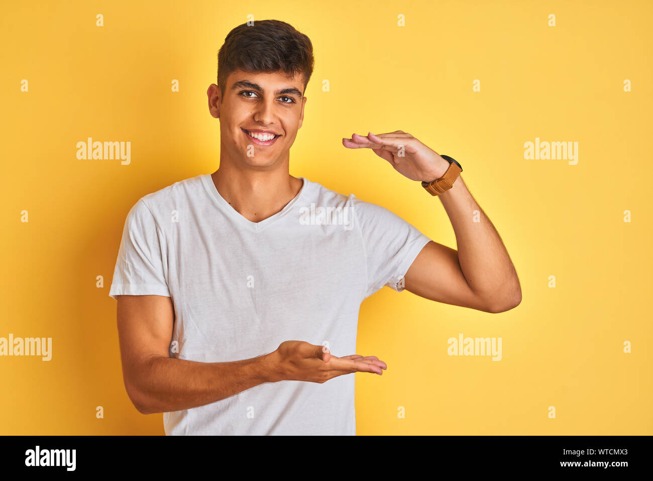 Young indian man wearing white t-shirt standing over isolated yellow ...