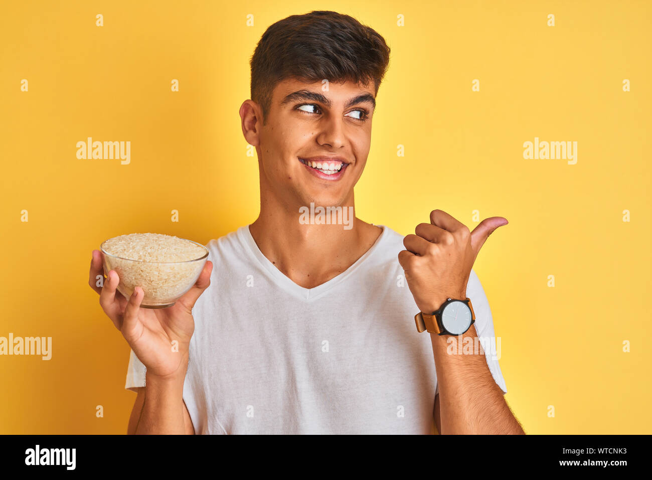 Young indian man holding bowl with rice standing over isolated yellow ...