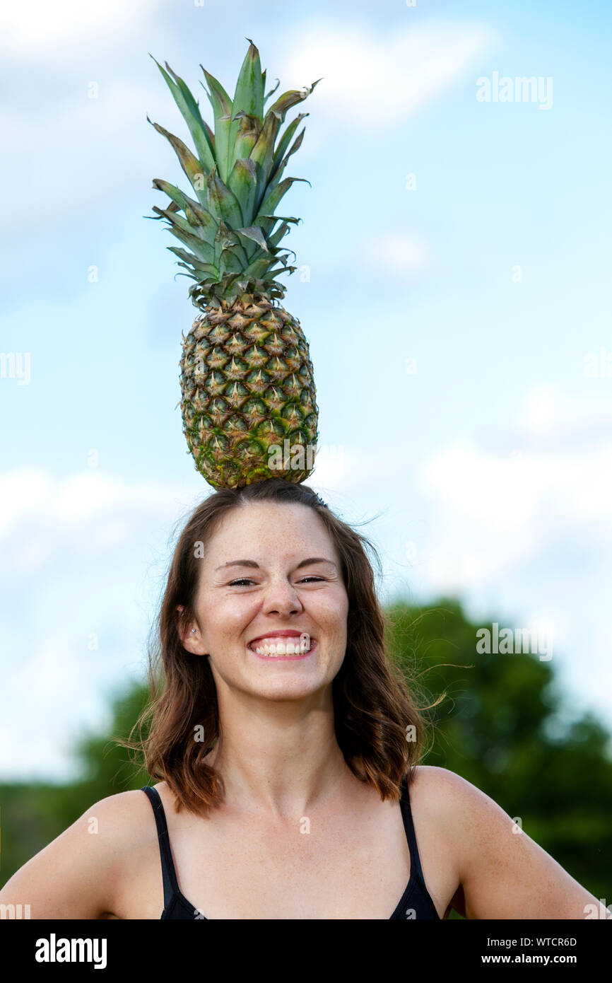 portrait of young woman balancing a pineapple on her head