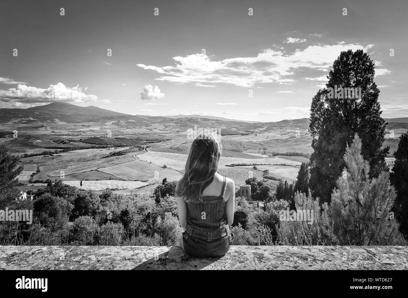 Rear View Of Young Woman Sitting On Retaining Wall At Val D Orcia Stock Photo