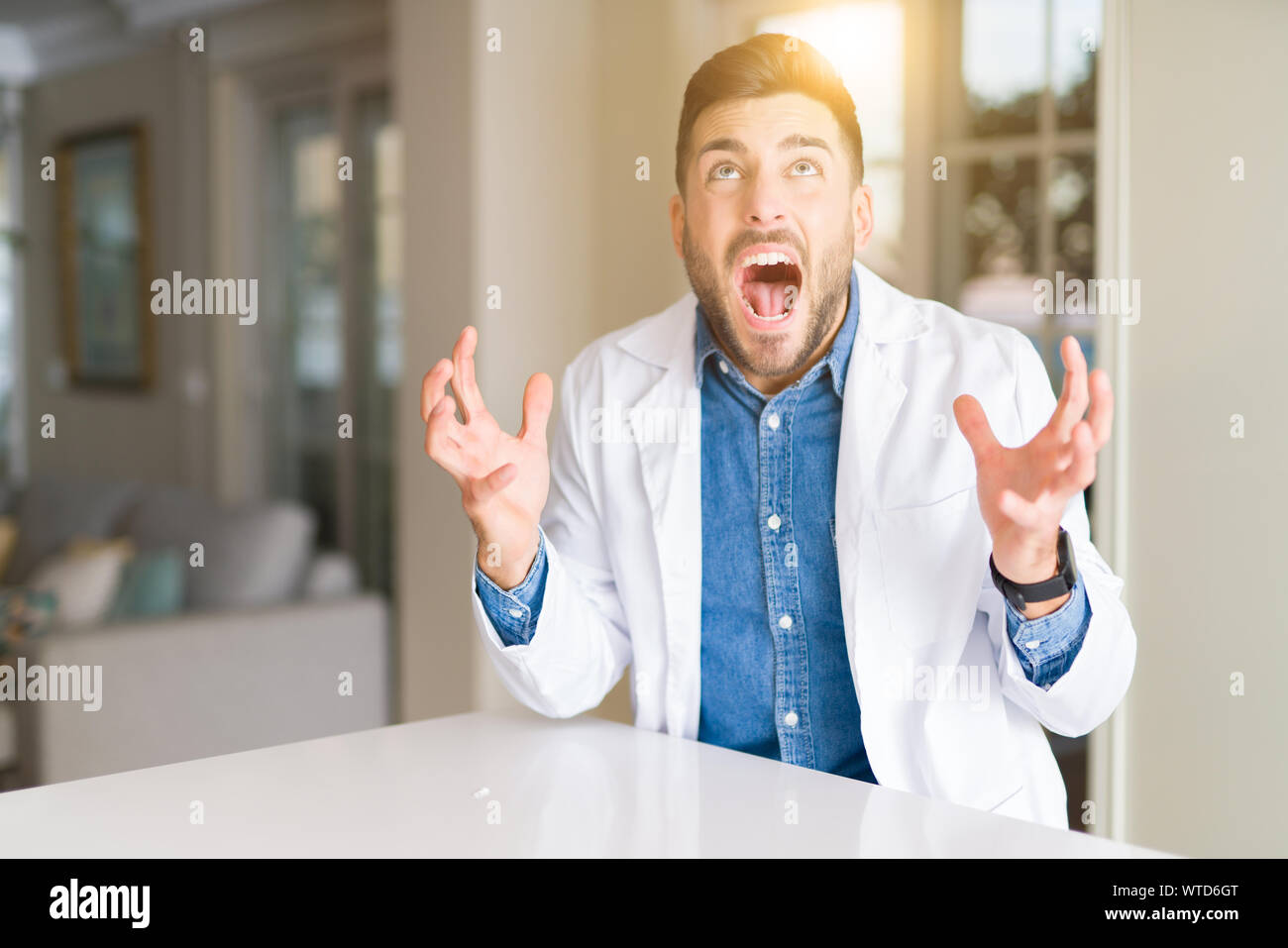 Young handsome doctor man at the clinic crazy and mad shouting and ...