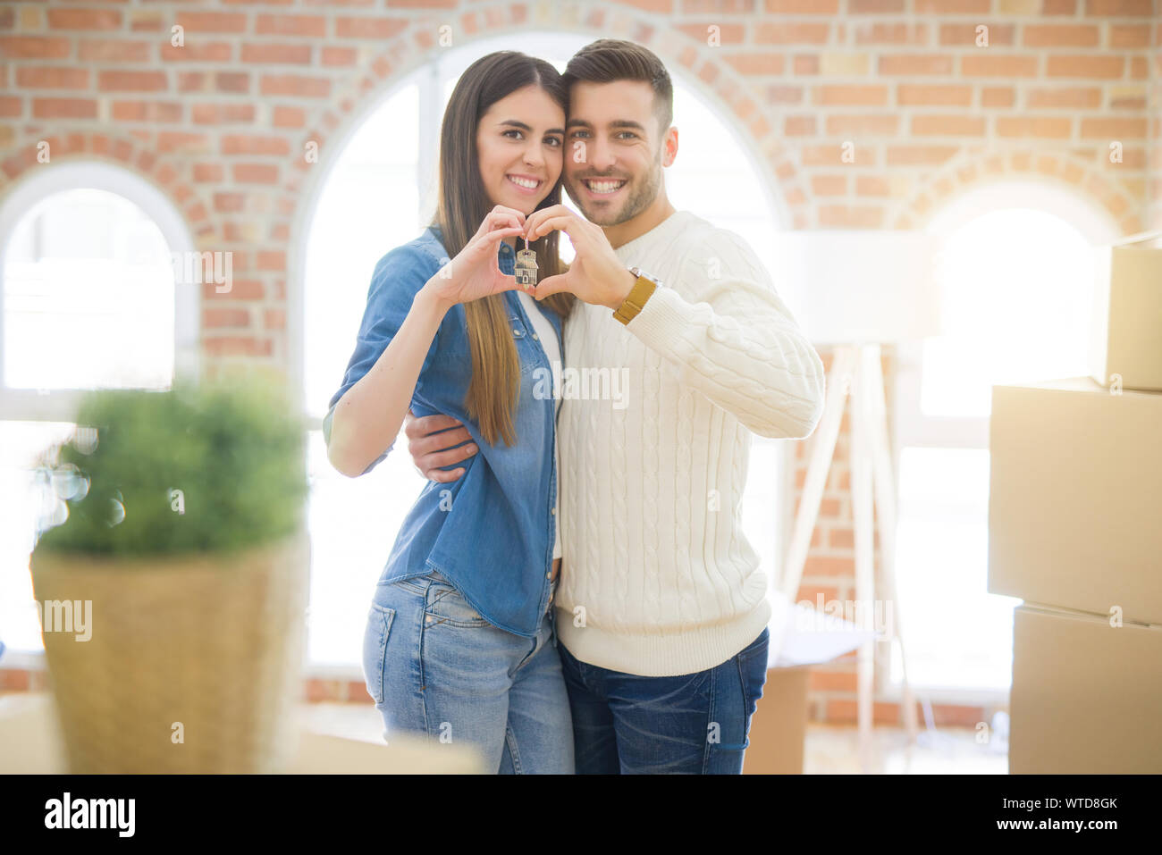 Young couple moving to a new home, hugging in love showing keys of new ...