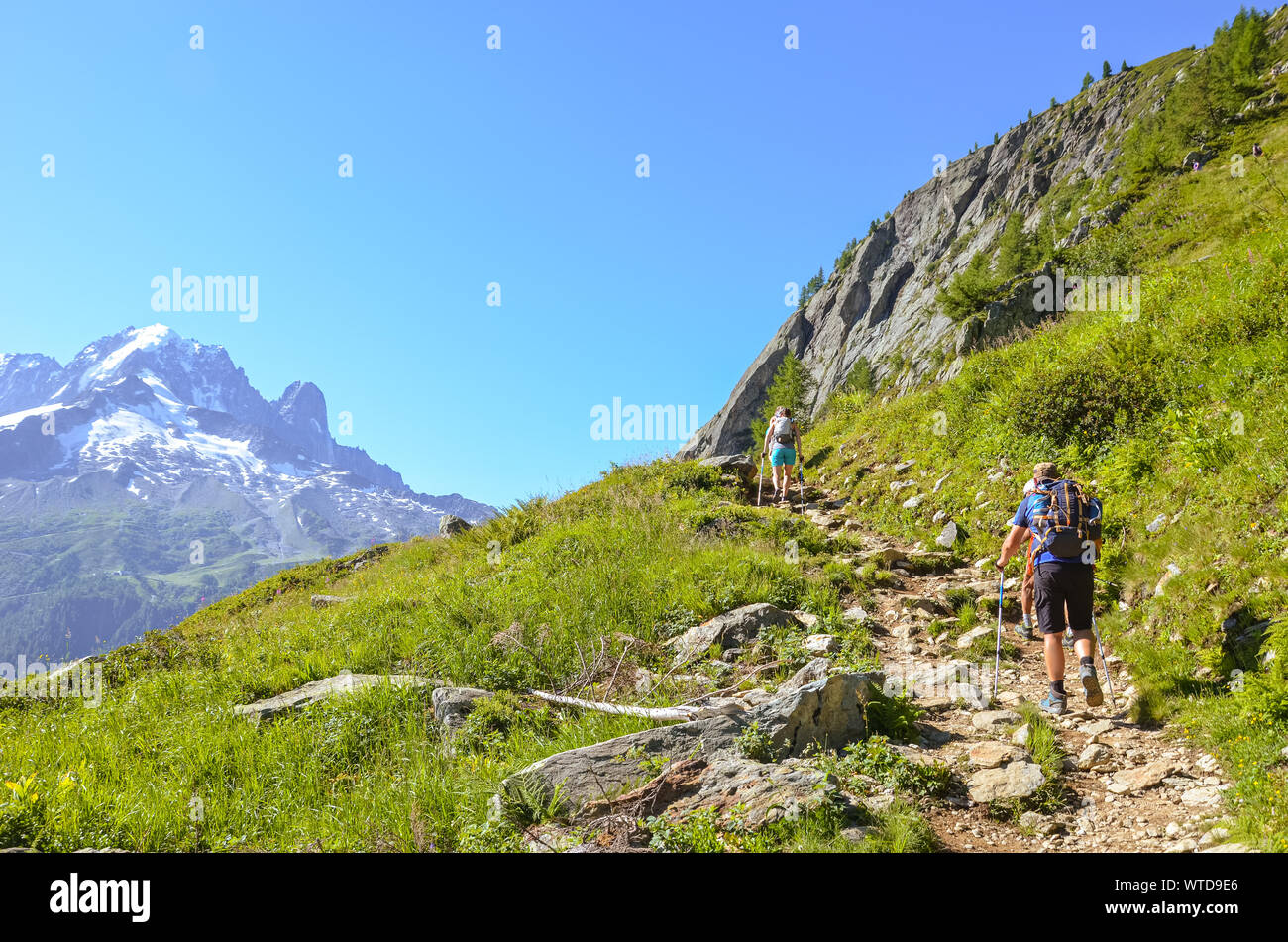Hikers with hiking poles in French Alps near Chamonix on a trail to Lac Blanc with Mont Blanc view. Beautiful Alpine landscape in France. People with walking sticks. Alps in summer. Active vacation. Stock Photo
