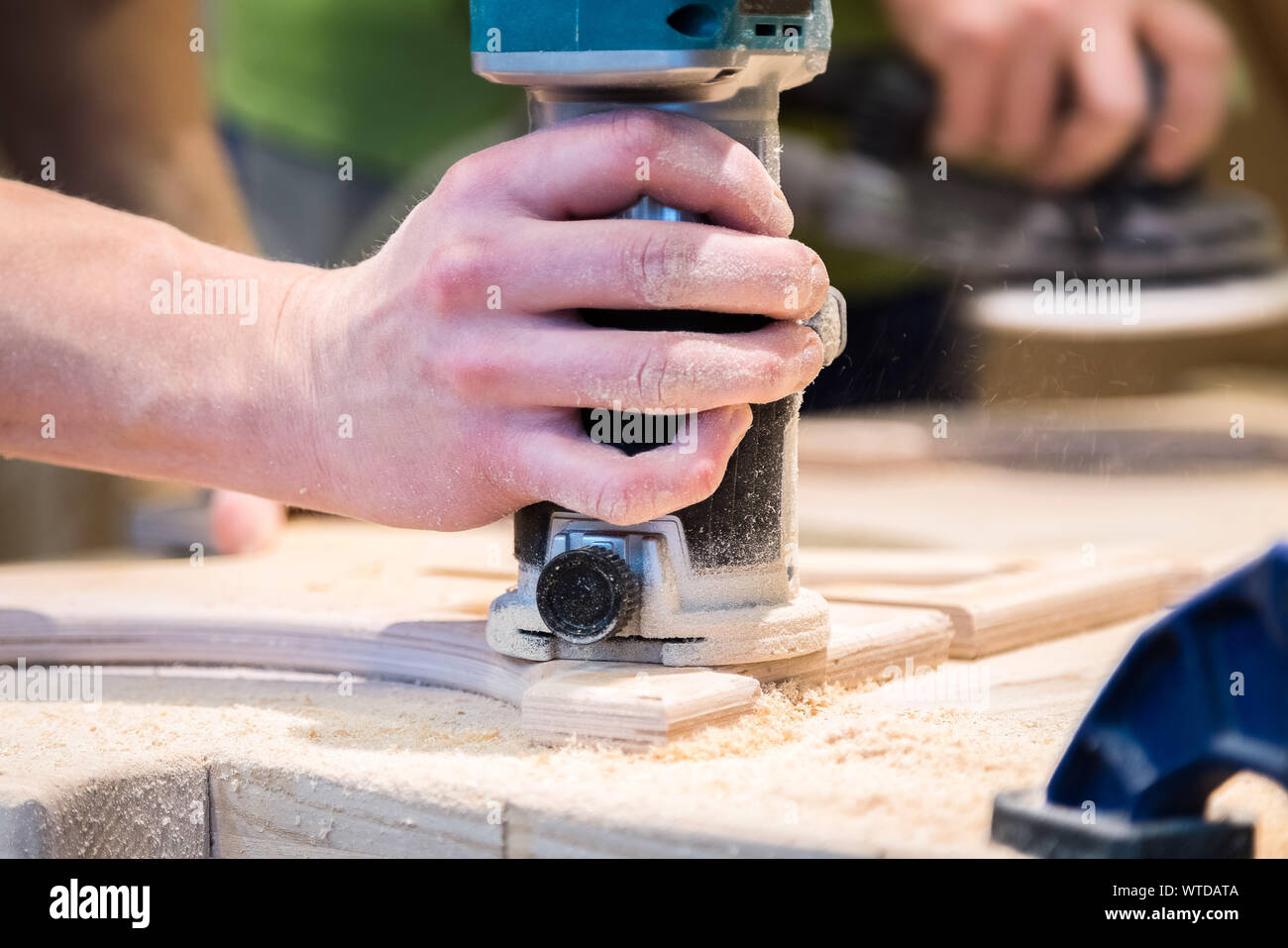 Young carpenter grinding cut out food decoration with electric ...