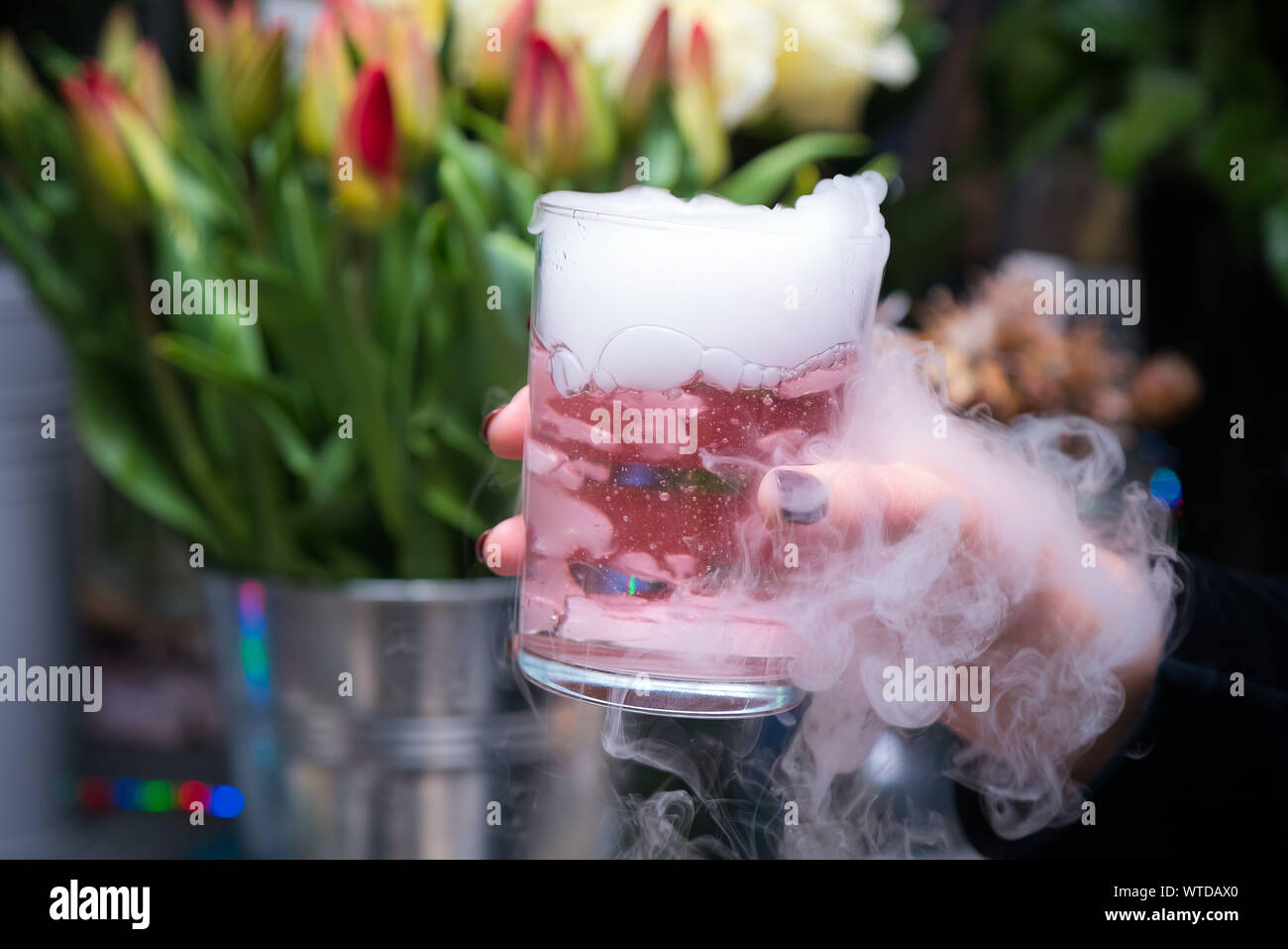 Beautiful woman holding dry ice cocktail at the party. Purple cocktail drink with ice vapor at the club Stock Photo