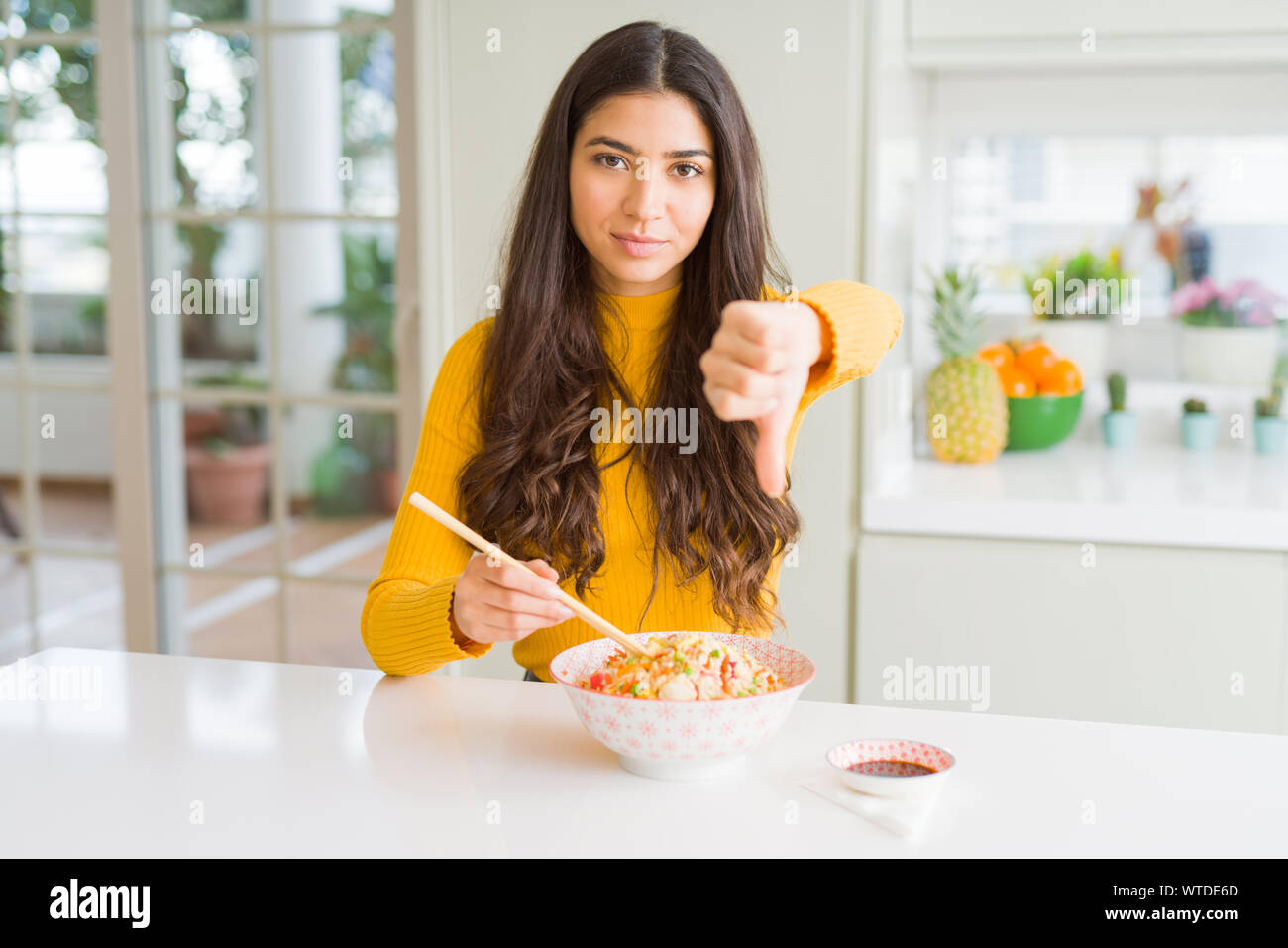 Young woman eating a bowl of Asian rice using chopsticks with angry ...