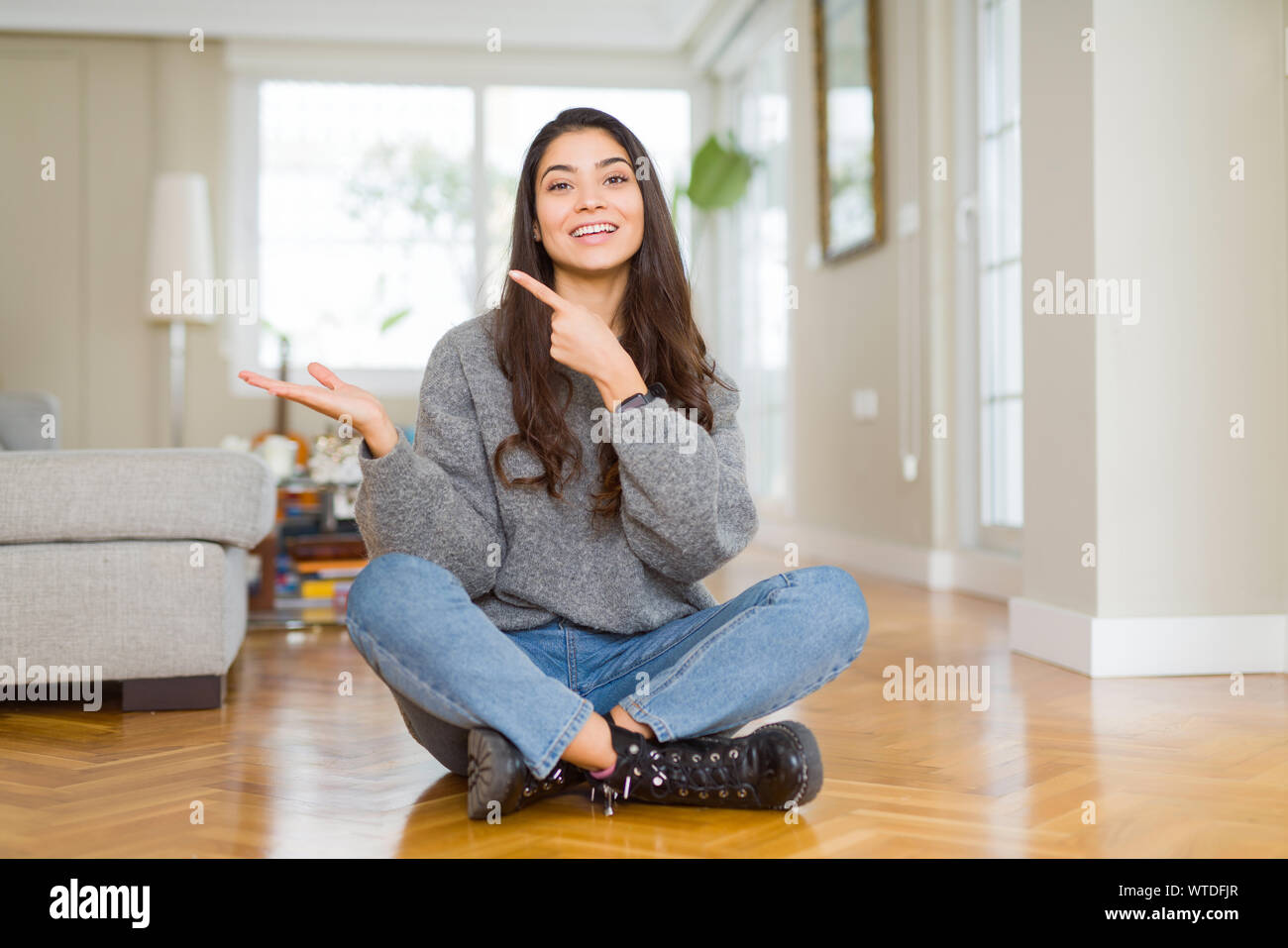 Young beautiful woman sitting on the floor at home amazed and smiling ...