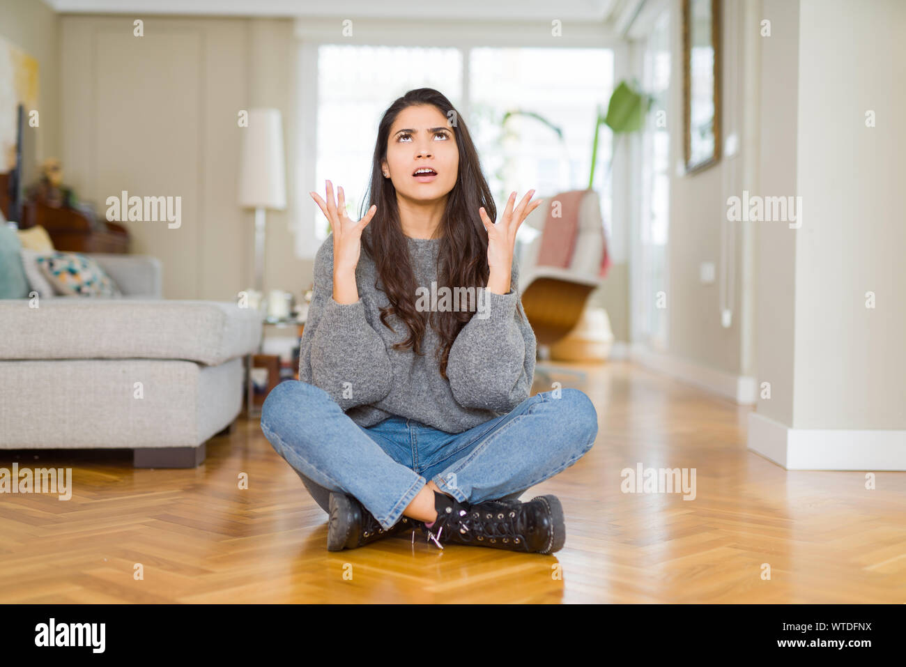 Young beautiful woman sitting on the floor at home crazy and mad