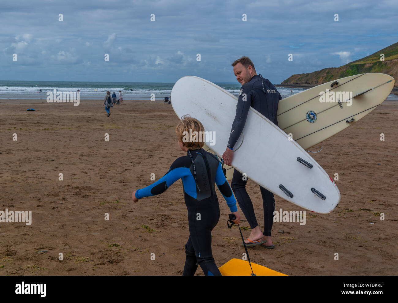 Father and son wearing wetsuits going surfing on the  Saunton Sands, North Devon, England, UK Stock Photo