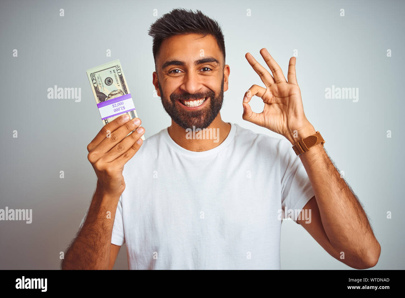 Young indian man holding dollars standing over isolated white ...