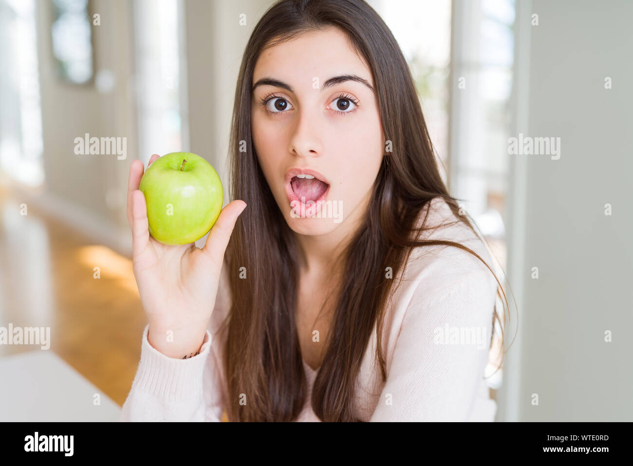 Beautiful young woman eating healthy green apple fruit scared in shock ...